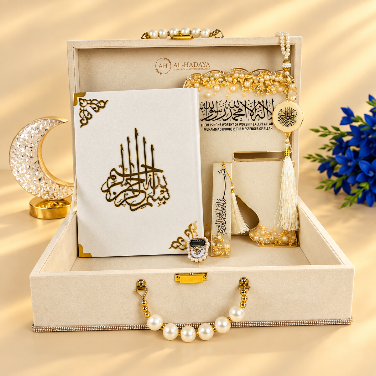 An open luxury gift box set for Eid Mubarak, featuring a white calligraphy greeting card, gold and white tassel ornaments, pearl jewelry, a gold crescent moon stand, and a small decorative pouch, all arranged on a beige satin background.