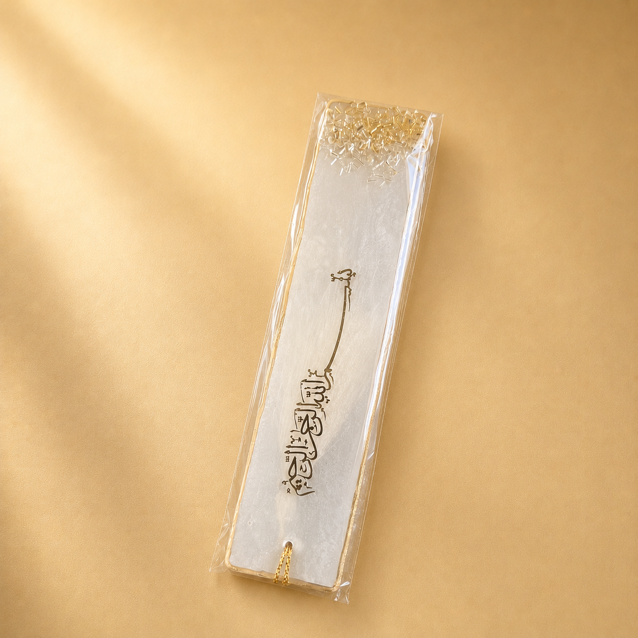 Silver bookmark with gold accents in clear packaging on a gold background