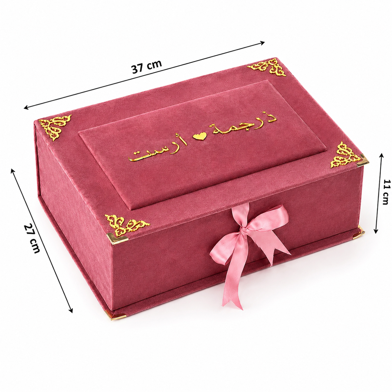 A red velvet jewelry box with gold corner accents and Arabic script on the lid, shown with pink ribbon bow and dimension lines indicating 37 cm length, 27 cm width, 11 cm height, and 1 cm thickness on a white background.