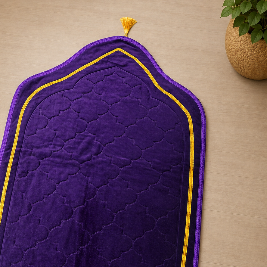 A purple prayer mat with gold trim and fringe, laid out on a light wood floor next to a potted plant.