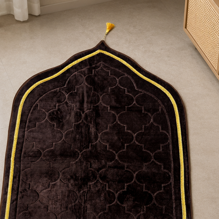 A dark brown velvet prayer rug with a geometric trellis pattern, a yellow border, and a matching yellow tassel and fringe, laid out on a beige tiled floor.