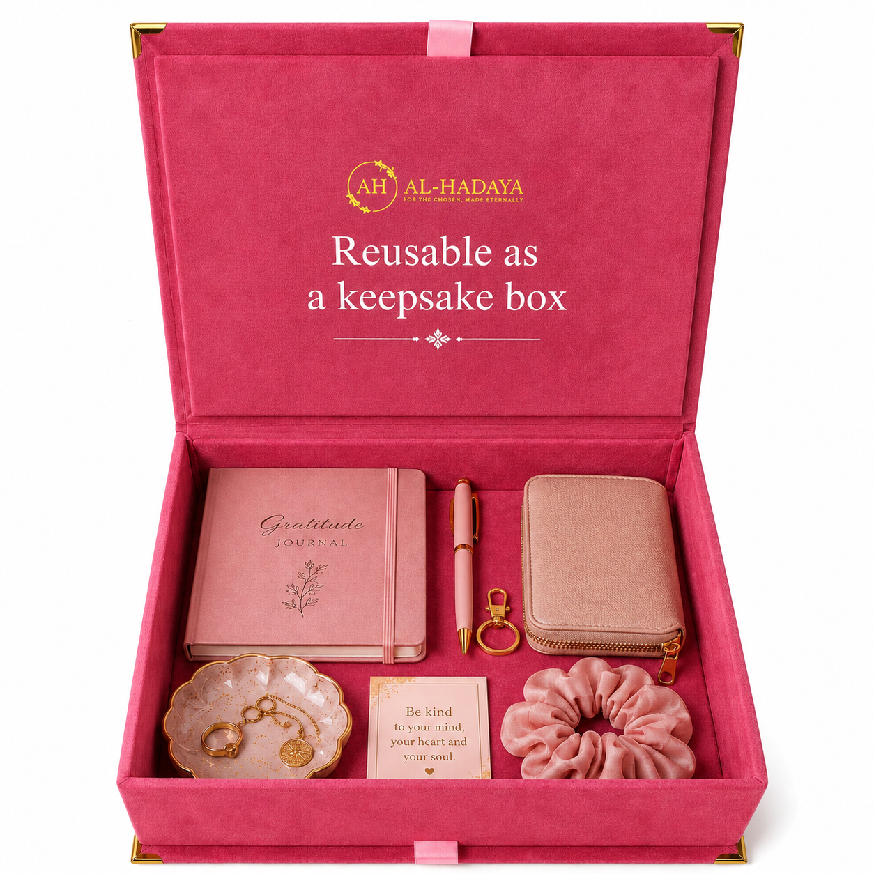 An open pink keepsake gift box with gold trim, branded 'AH AL-HADAYA', containing a pink journal, matching pen, zip wallet, small jewelry dish with gold-tone earrings, a card, and a pink scrunchie. The inside lid reads 'Reusable as a keepsake box'.