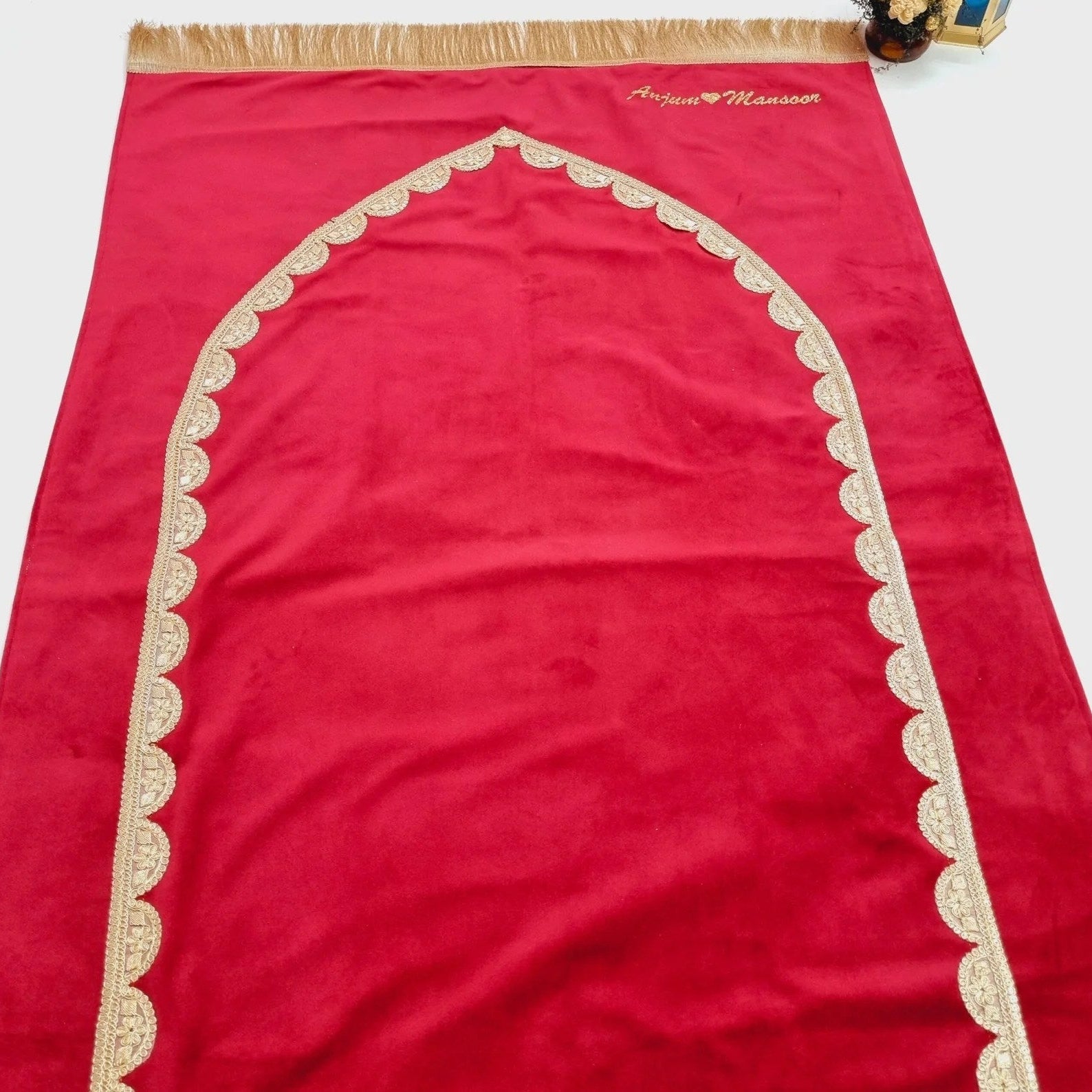 Regal maroon velvet prayer rug with gold lace and personalized touch.