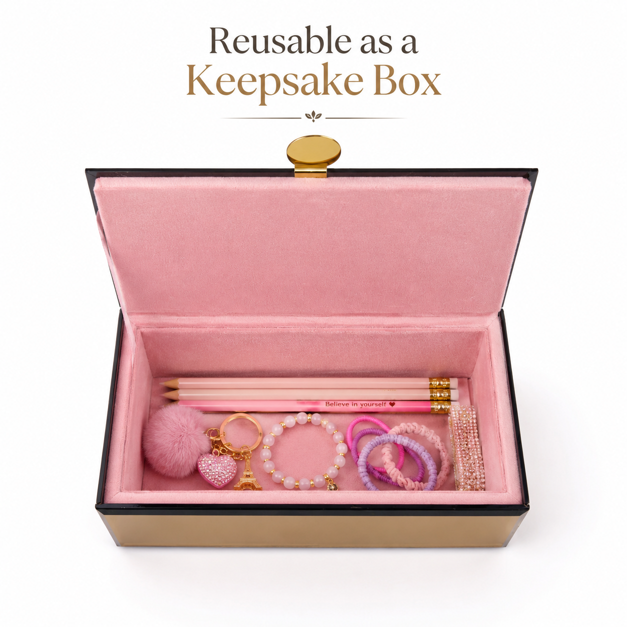 An open pink velvet keepsake box with a black border and gold clasp, shown on a white background with the text 'Reusable as a Keepsake Box' above it. Inside, pastel jewelry accessories including a pink pom-pom, beaded keychain, rings, bracelets, and a pencil are arranged.