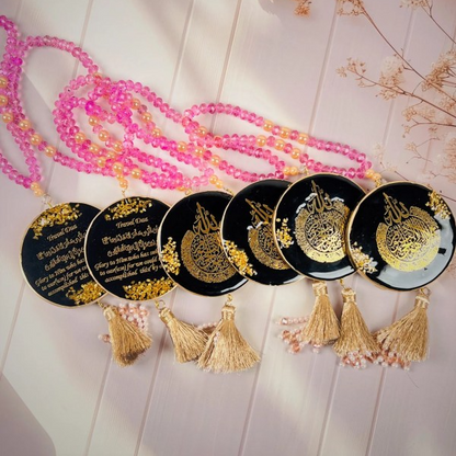 Islamic car hanger with Travel Dua in gold calligraphy on black resin pendant, decorated with pink and peach beads, gold tassel, and pearl accents.