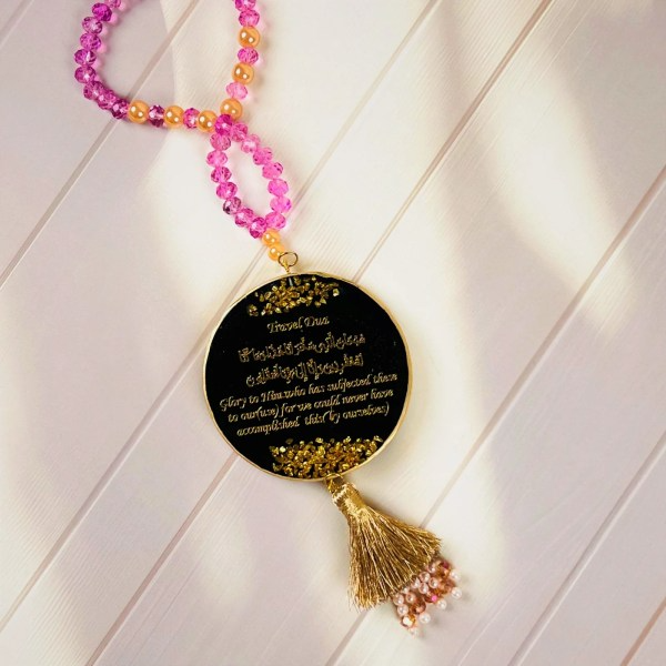 Islamic car hanger with Travel Dua in gold calligraphy on black resin pendant, decorated with pink and peach beads, gold tassel, and pearl accents.