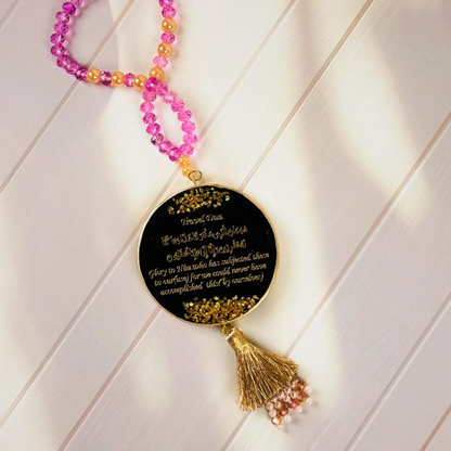 Islamic car hanger with Travel Dua in gold calligraphy on black resin pendant, decorated with pink and peach beads, gold tassel, and pearl accents.