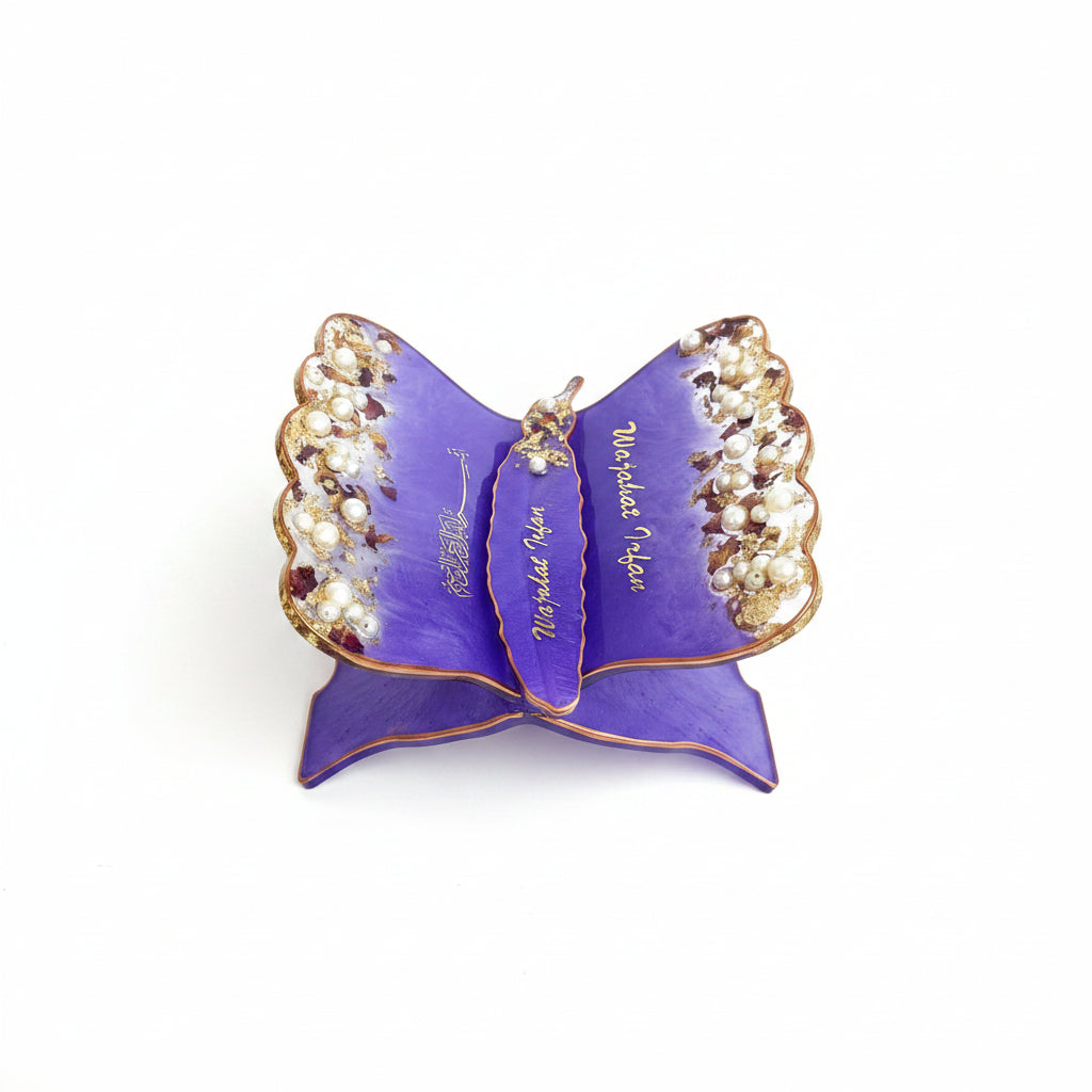A purple butterfly-shaped jewelry stand with gold trim and pearl embellishments, displayed on a white faux fur surface.
