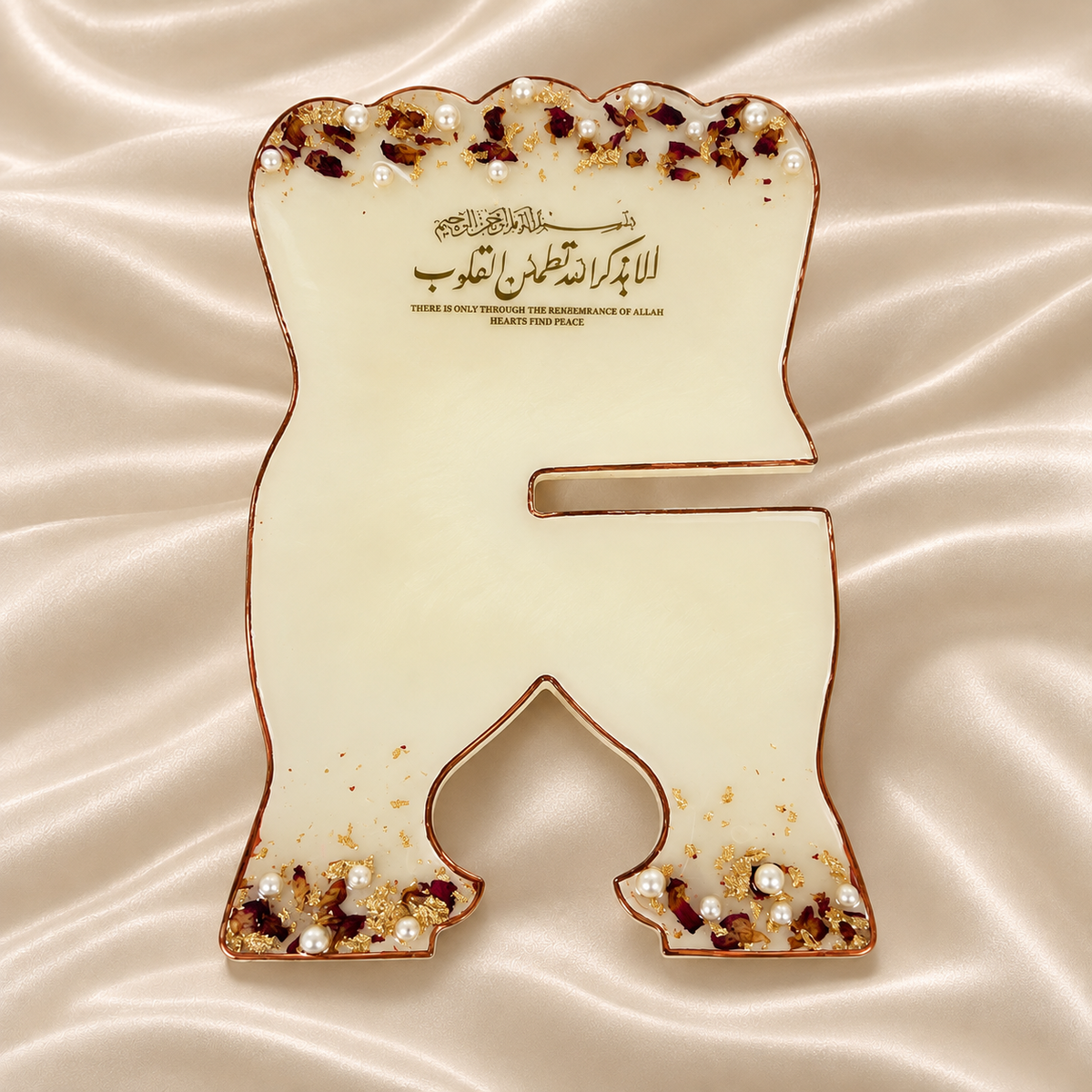 A premium resin rehal displayed open on a cream satin background, featuring elegant gold Arabic calligraphy, delicate rose petals, pearl embellishments, gold flakes, and a metallic border. The image highlights its elegant design, beautiful calligraphy, sturdy construction, and premium resin finish.