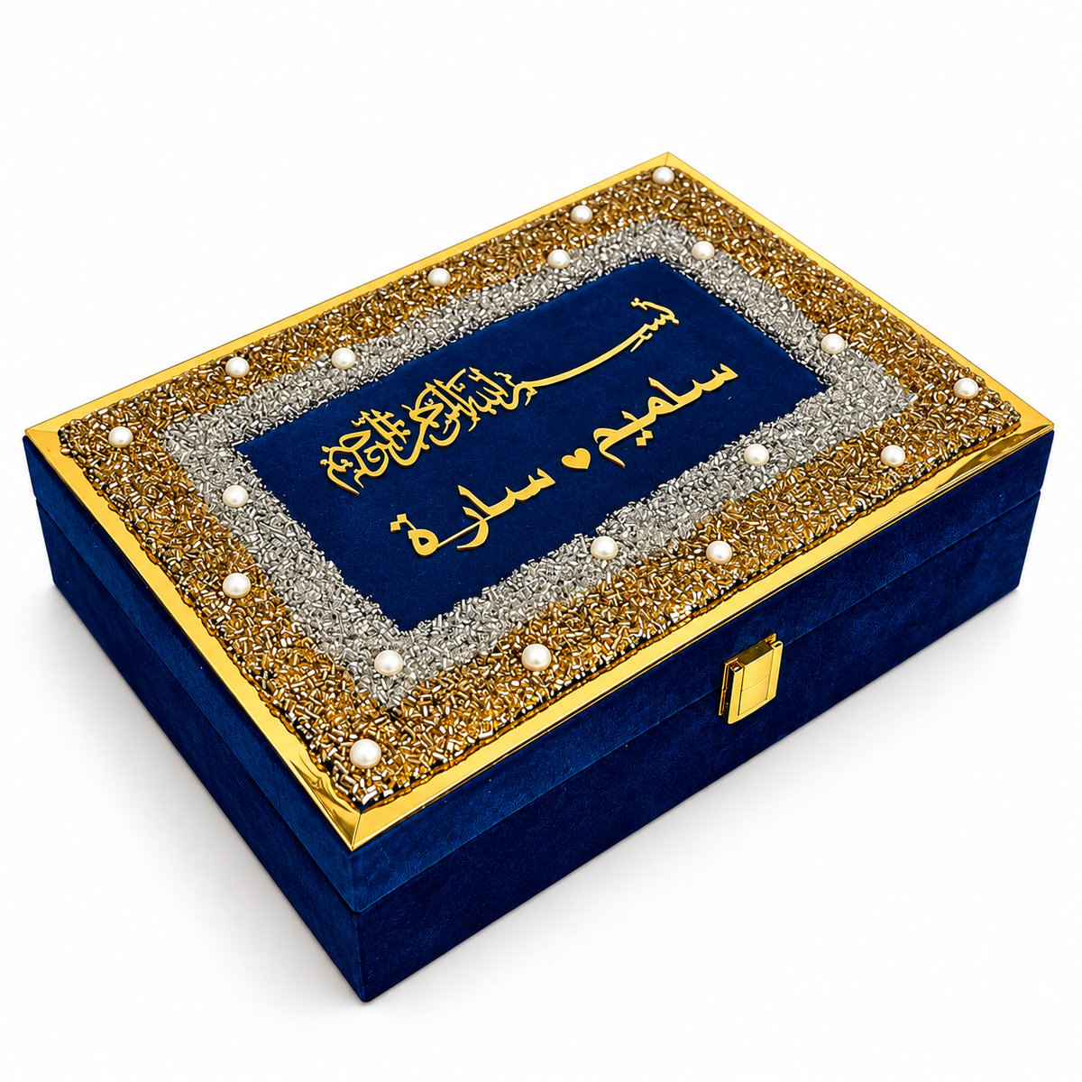 A rectangular velvet box in deep blue, decorated with a gold and silver beaded border and white pearl-like accents on the lid. The lid features gold Arabic calligraphy on a dark blue panel.