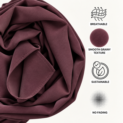 A close-up of draped burgundy fabric on a white background with feature icons and text reading Breathable, Smooth Grainy Texture, Sustainable, and No Fading.