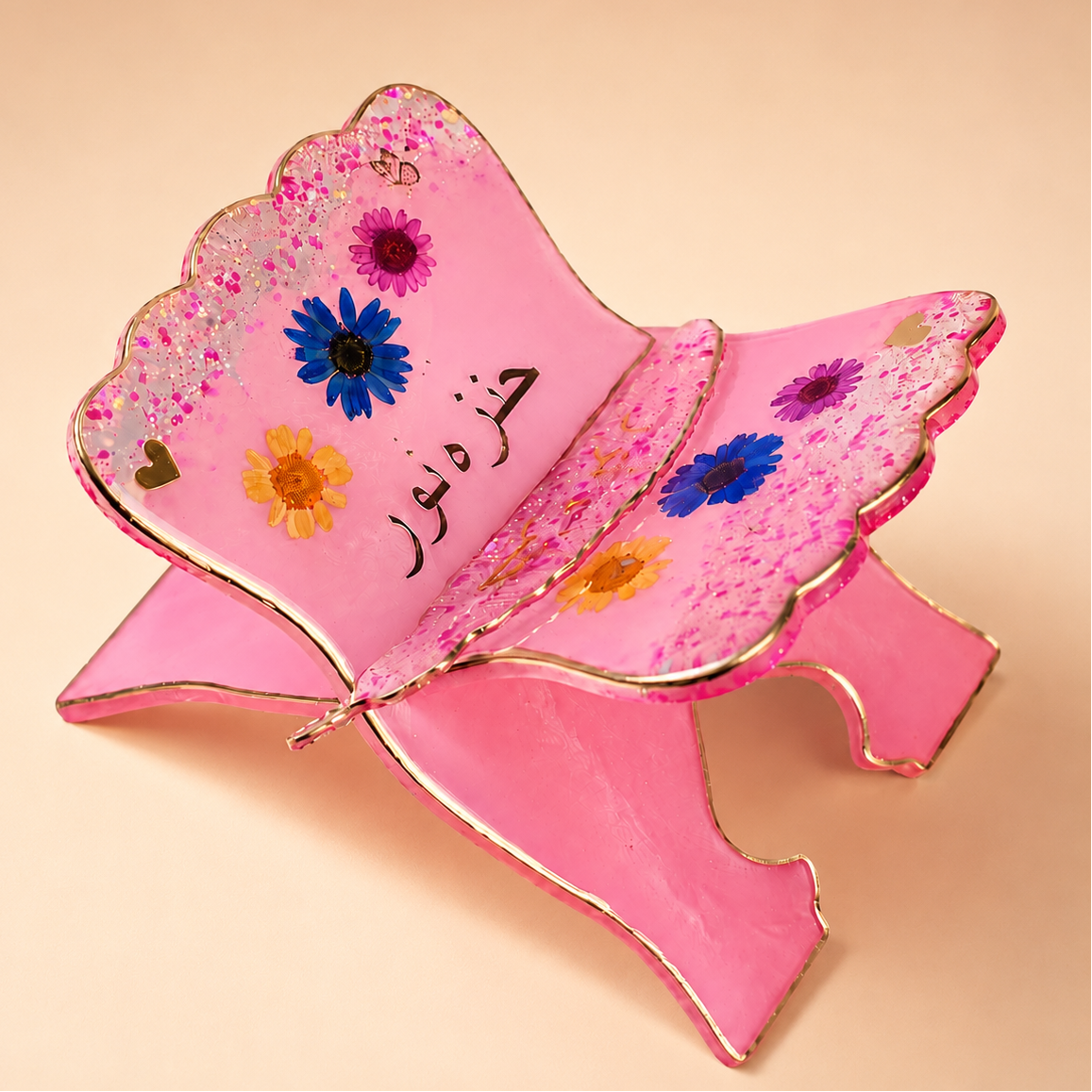 Pink decorative item with floral designs and Arabic text on a beige background