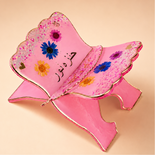 Pink decorative item with floral designs and Arabic text on a beige background