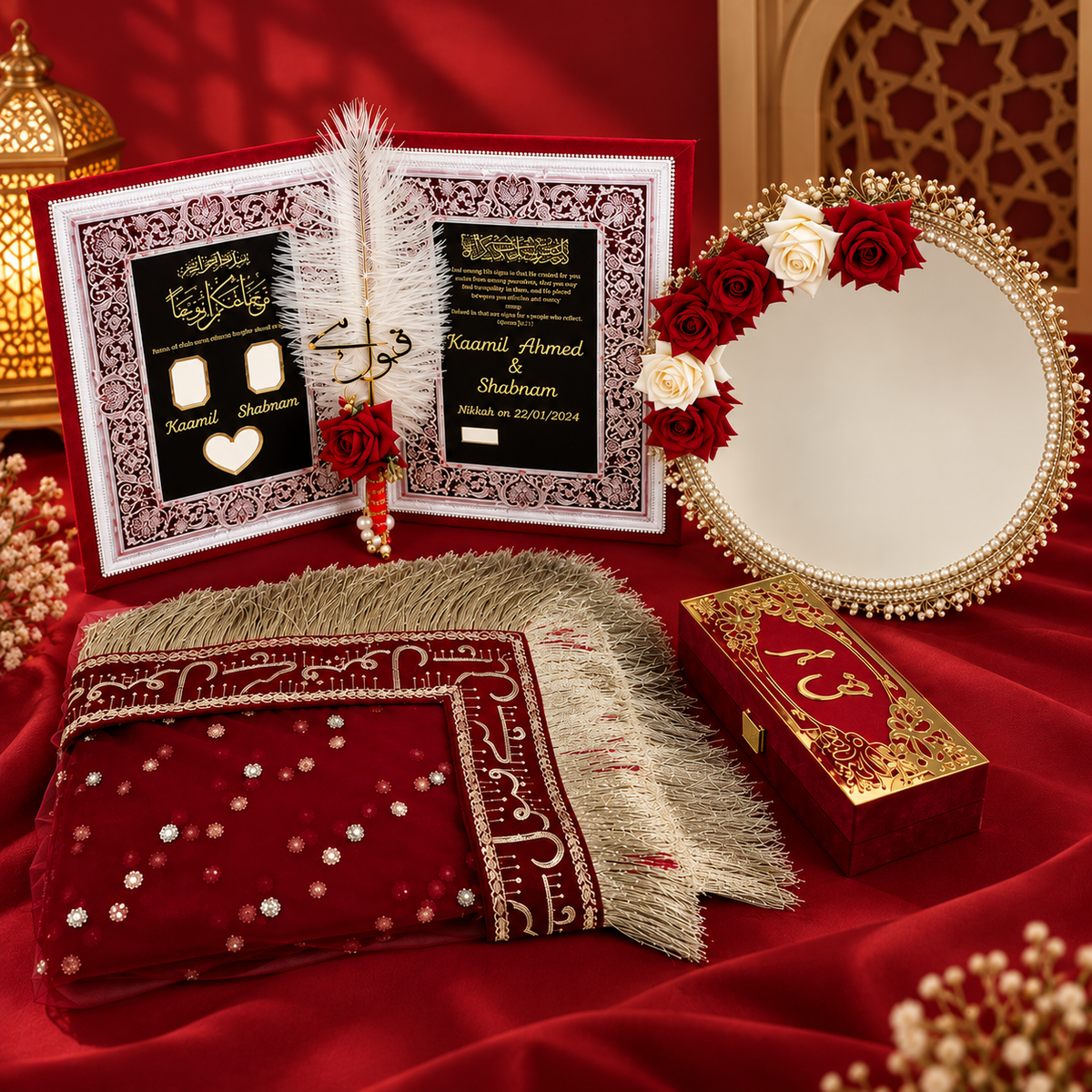 A traditional Islamic wedding set arranged on a rich red fabric backdrop. The set includes an open wedding invitation book with gold and black calligraphy on a red cover, a red and gold embroidered prayer mat, a small red and gold keepsake box, a decorative mirror adorned with red and white roses, and a gold lantern.