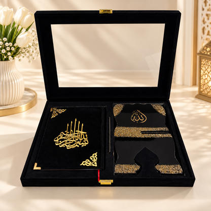 A luxury black velvet Islamic gift set displayed in an open presentation box. The set includes a black velvet notebook with gold Arabic calligraphy, a black prayer rug with gold patterns, a black prayer shawl, and a black pen, all decorated with intricate gold foil designs.