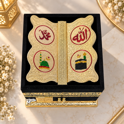 A decorative black and gold keepsake box with two butterfly-shaped gold inserts featuring red Arabic calligraphy and small illustrated motifs, displayed on a marble surface with floral props.