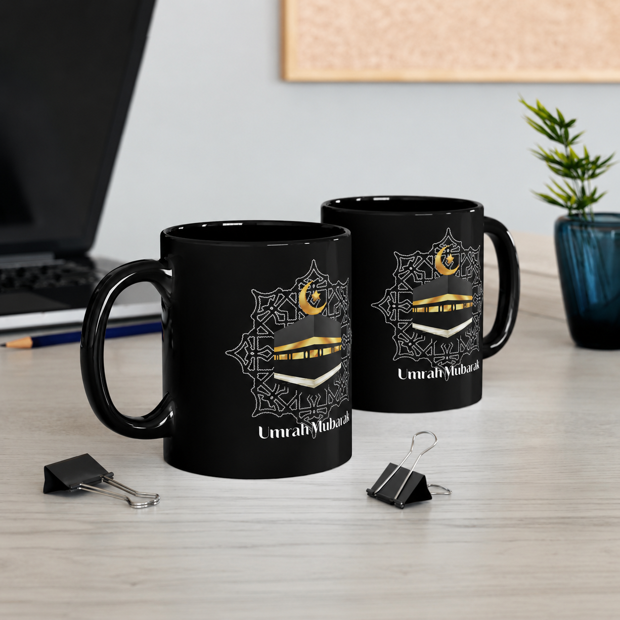 Two black mugs with gold and white designs on a desk with office supplies.
