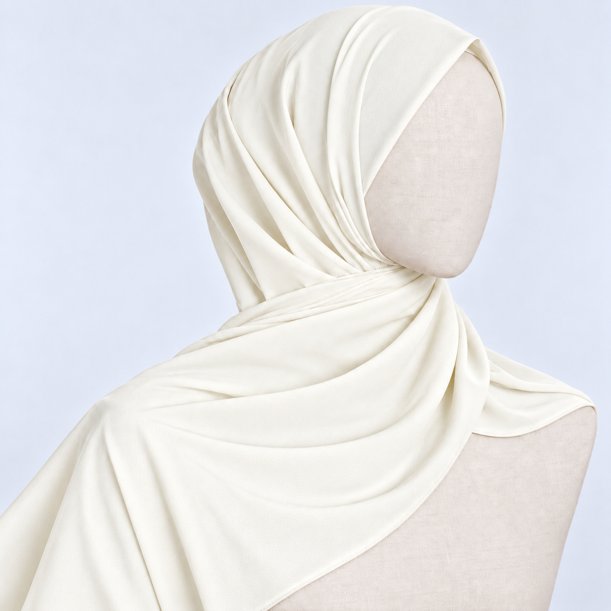 An off-white hijab draped elegantly on a mannequin head and shoulders against a light blue background.