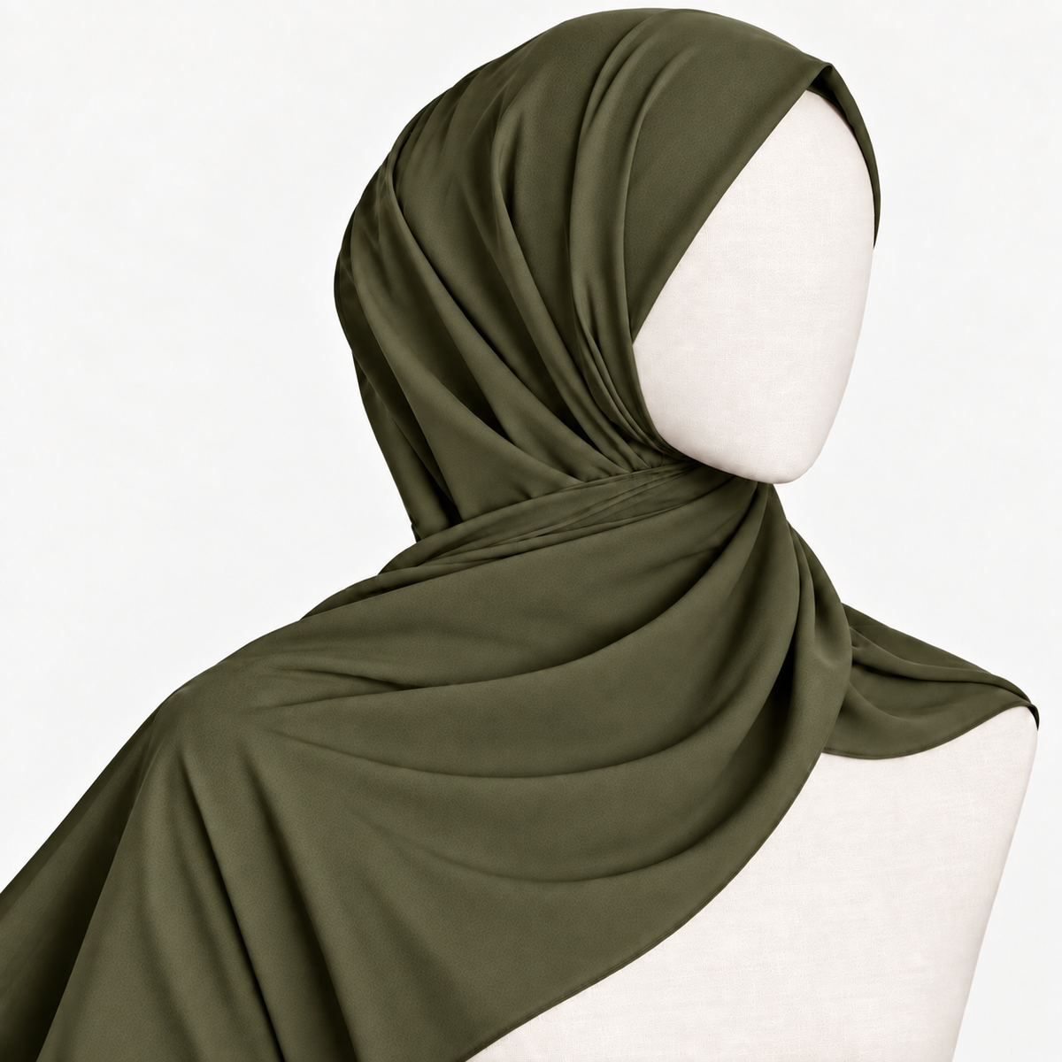 A woman wearing a draped olive green hijab and a white embroidered blouse, posed against a light gray studio background.