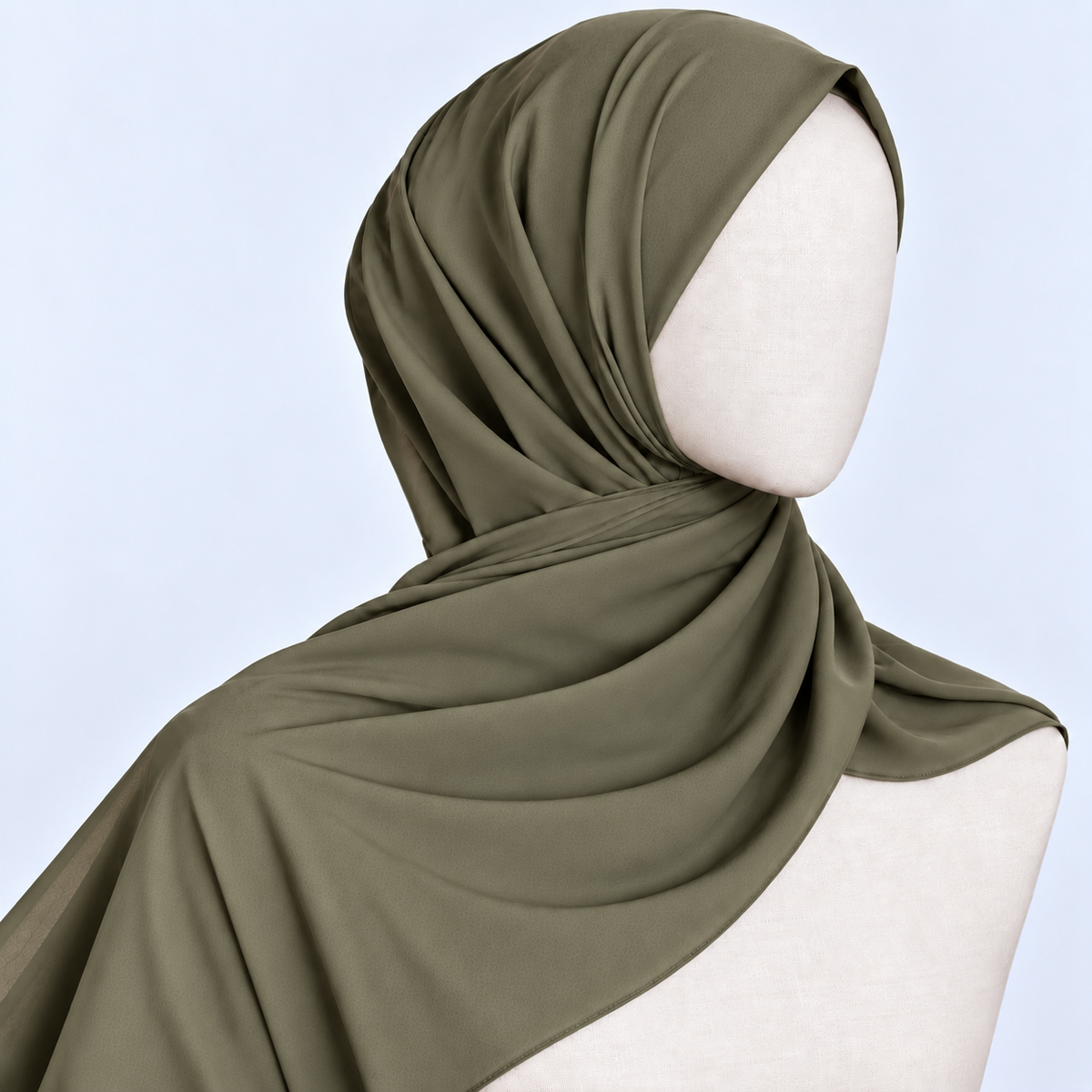 An olive green hijab draped elegantly on a cream-colored mannequin head and shoulders against a light blue background.
