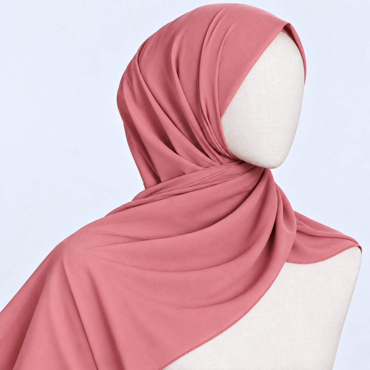 A dusty rose pink hijab draped elegantly on a white mannequin head and shoulders against a light blue background.