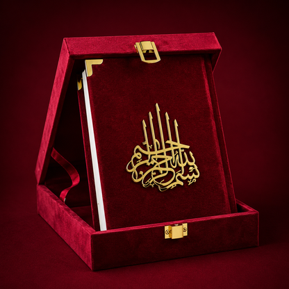 A gold-tone Islamic calligraphy plaque   presented inside an open red velvet book-shaped gift box with gold corner accents and clasps, set against a dark red background.
