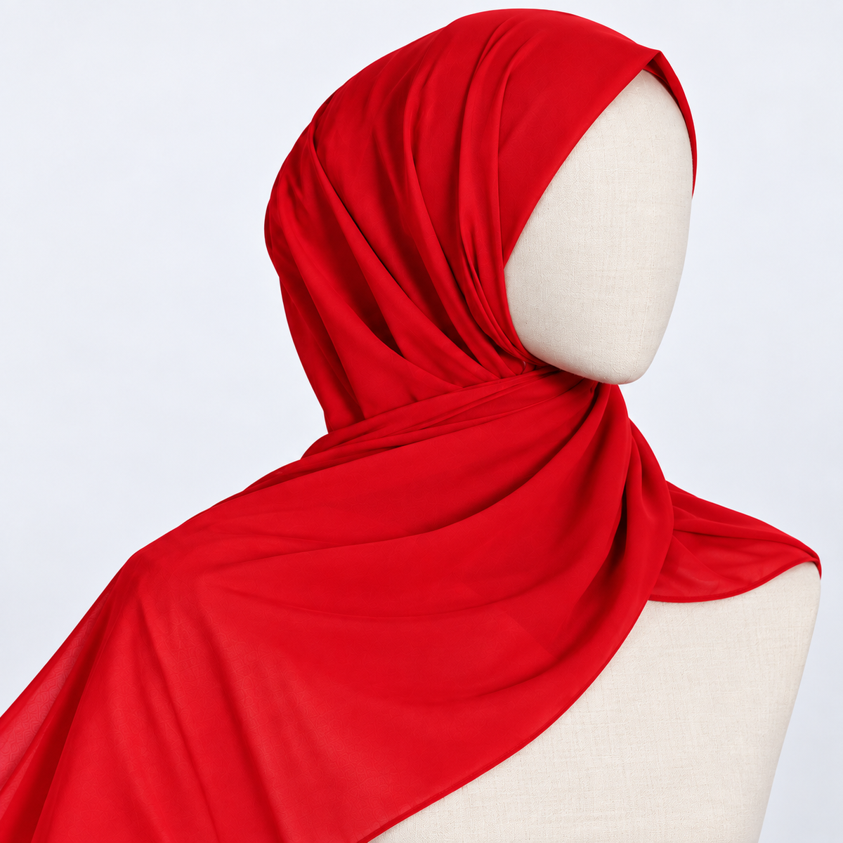 A bright red hijab draped on a cream-colored mannequin torso against a light gray background.