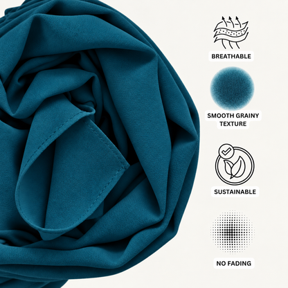 A close-up of teal-blue fabric with a soft grainy texture, shown in draped folds on a light background with feature icons and text reading Breathable, Smooth Grainy Texture, Sustainable, and No Fading.