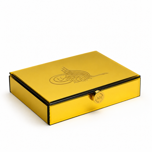 A rectangular metallic gold box with a hinged lid, featuring an embossed crescent and star design on the top and a small round gold clasp on the front, shown on a clean white background.
