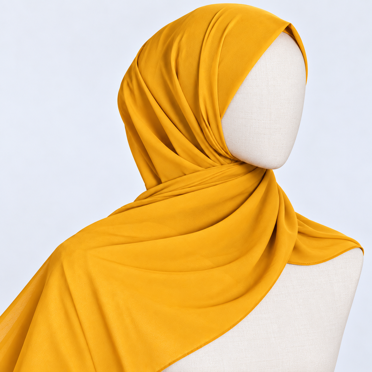 A mustard yellow hijab draped elegantly on a white mannequin head and shoulders against a light gray studio background.